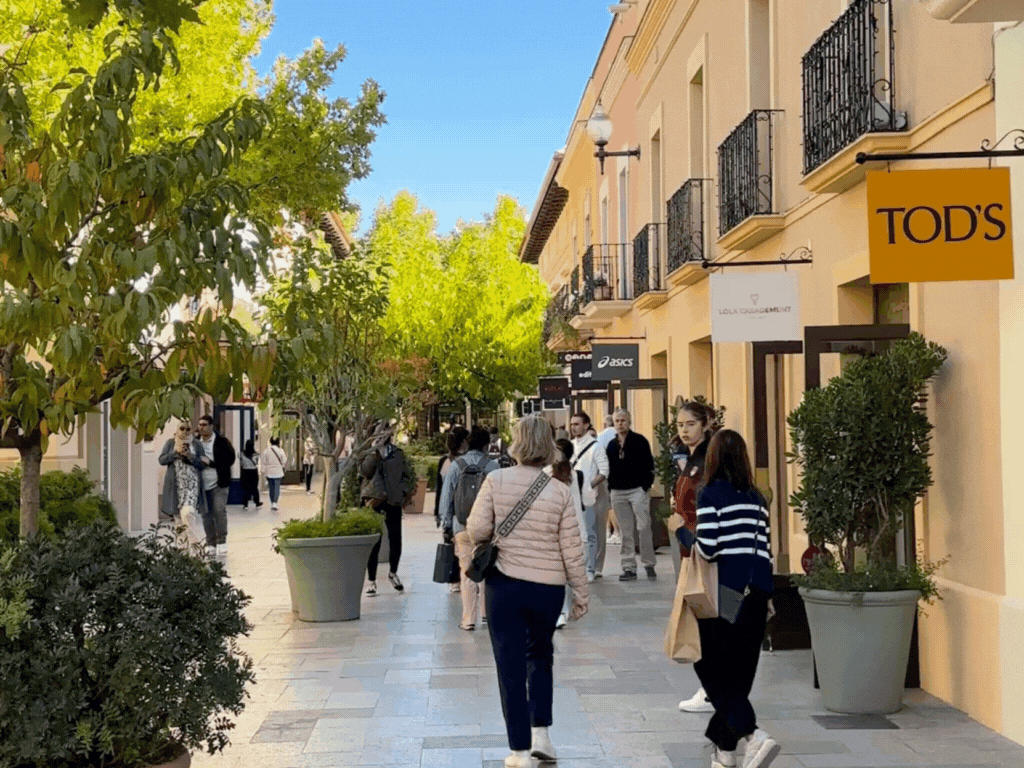 拉罗卡购物村内部景观，背景是通往 Asics 商店的宽阔人行道，周围是其他精品店和雅致的装饰。.