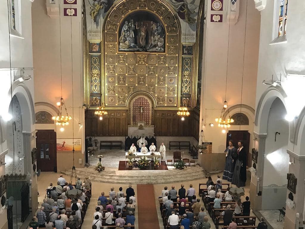 Misa en curso dentro de la Iglesia de Sant Joan de Gràcia, con fieles participando y altar al fondo.
