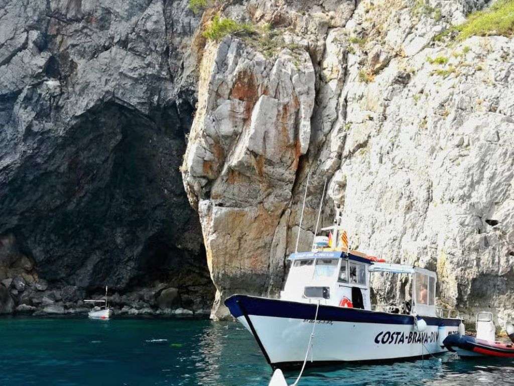 供教练和潜水初学者使用的小船停靠在蒙特格里(Montgrí)水域中的一些岩石前,这些岩石形成了环绕海滩的岩石斜坡。.