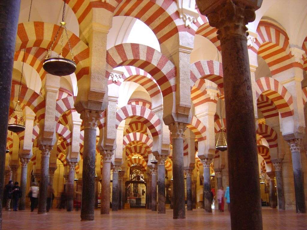 Foto interior de la Mezquita de Córdoba con su influencia del Al-Ándalus, con colores royos y blancos, arcos y columnas simples.