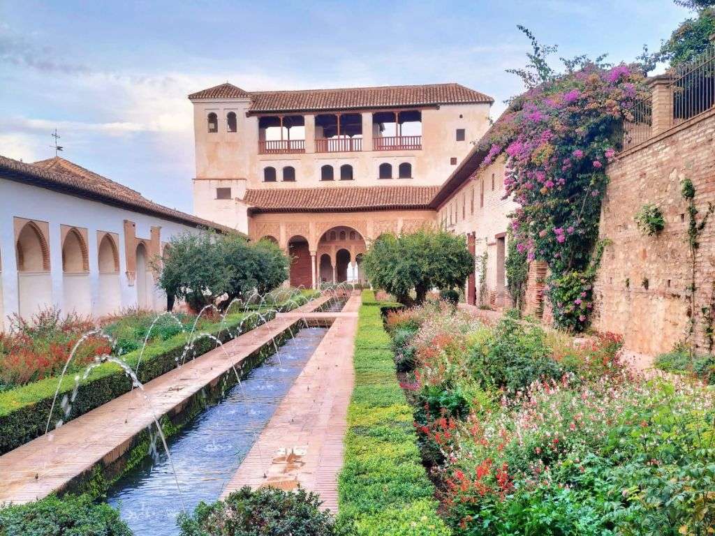 想象一下在阿尔罕布拉宫的一个标志性花园里，您可以看到房屋建筑、带有喷泉的人行道以及周围的植被。.