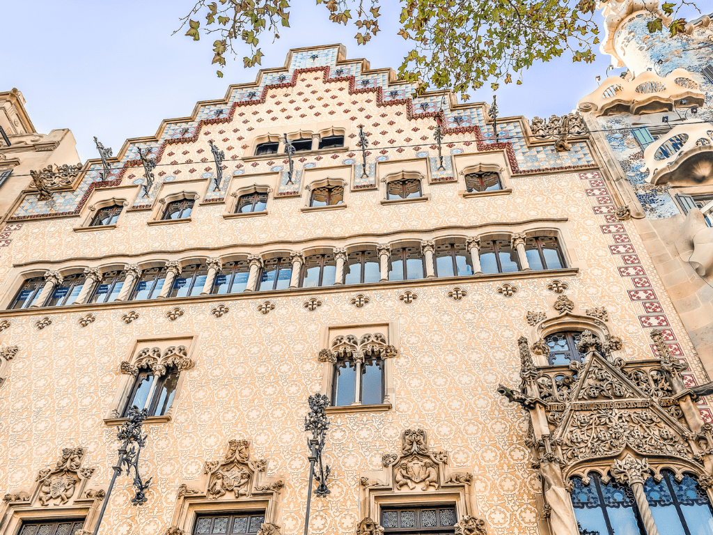 Vista frontal de la Casa Amatller en Barcelona, mostrando su distintiva fachada de estilo modernista con influencias góticas y flamencas, adornada con azulejos coloridos, esculturas y el característico tejado escalonado