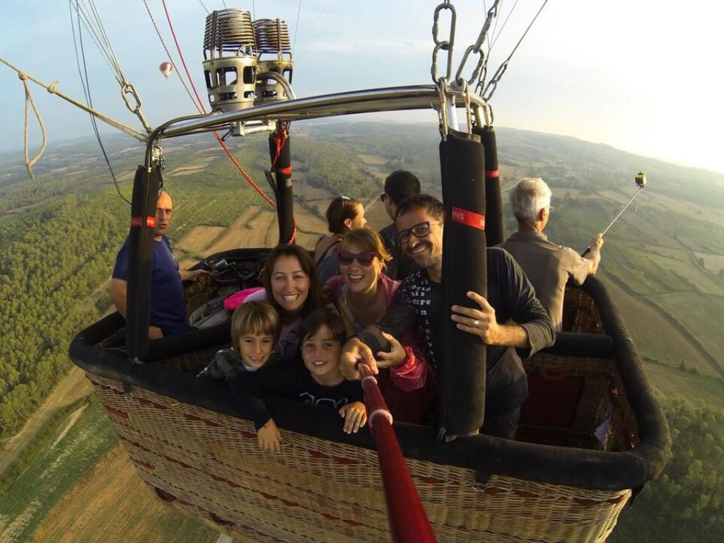 Una familia disfrutando de un emocionante vuelo en globo aerostático sobre el pintoresco paisaje del Empordà, Girona, con vistas panorámicas del entorno natural y cultural.