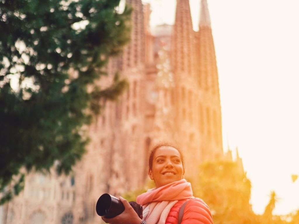 Vista de Barcelona capturada por una mujer con cámara frente a la Sagrada Familia, resaltando la arquitectura icónica y el vibrante ambiente urbano.